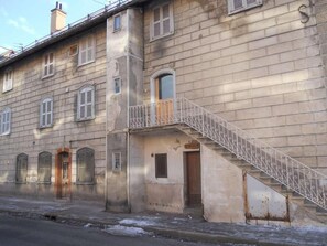 Un edificio con una scala che conduce a una porta, una piccola finestra e un balcone con ringhiera in metallo.