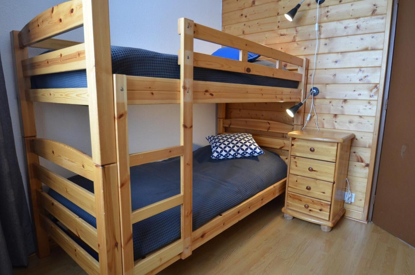 A bunk bed with a wooden frame, a small bedside table, and a lamp.