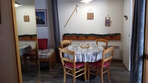 Un coin repas avec une table ronde, des chaises en bois et un banc. Un luminaire suspendu se trouve au-dessus de la table et une petite horloge est accrochée au mur.
