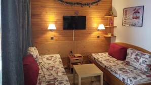 Une pièce chaleureuse aux murs en bois, avec deux canapés ornés de coussins à motifs, un téléviseur à écran plat et des lampes fixées au mur.