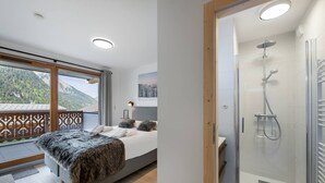 Ett modernt sovrum med en stor säng, en duschkabin i glas och en balkong med utsikt över bergen.