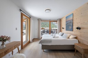 A bedroom with a large bed, wooden walls, a view of mountains, and a balcony with outdoor seating. - Close to the centre, new flat with 4 bedrooms and 3 bathrooms (CHATEL)