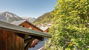 A wooden chalet with a view of a mountain village and forested hills.