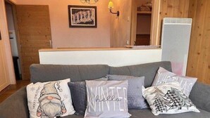A grey sofa with three decorative pillows, a framed artwork on the wall, and a heater unit to the right. - 100m from ski slopes, 3rd floor, view ski slopes, swimming pool, sauna, balcony, tv, ski locker (Risoul)