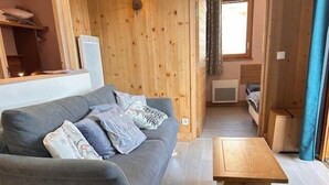 A cozy room with a grey sofa, wooden walls, a small wooden table, and a window with curtains. - 100m from ski slopes, 3rd floor, view ski slopes, swimming pool, sauna, balcony, tv, ski locker (Risoul)