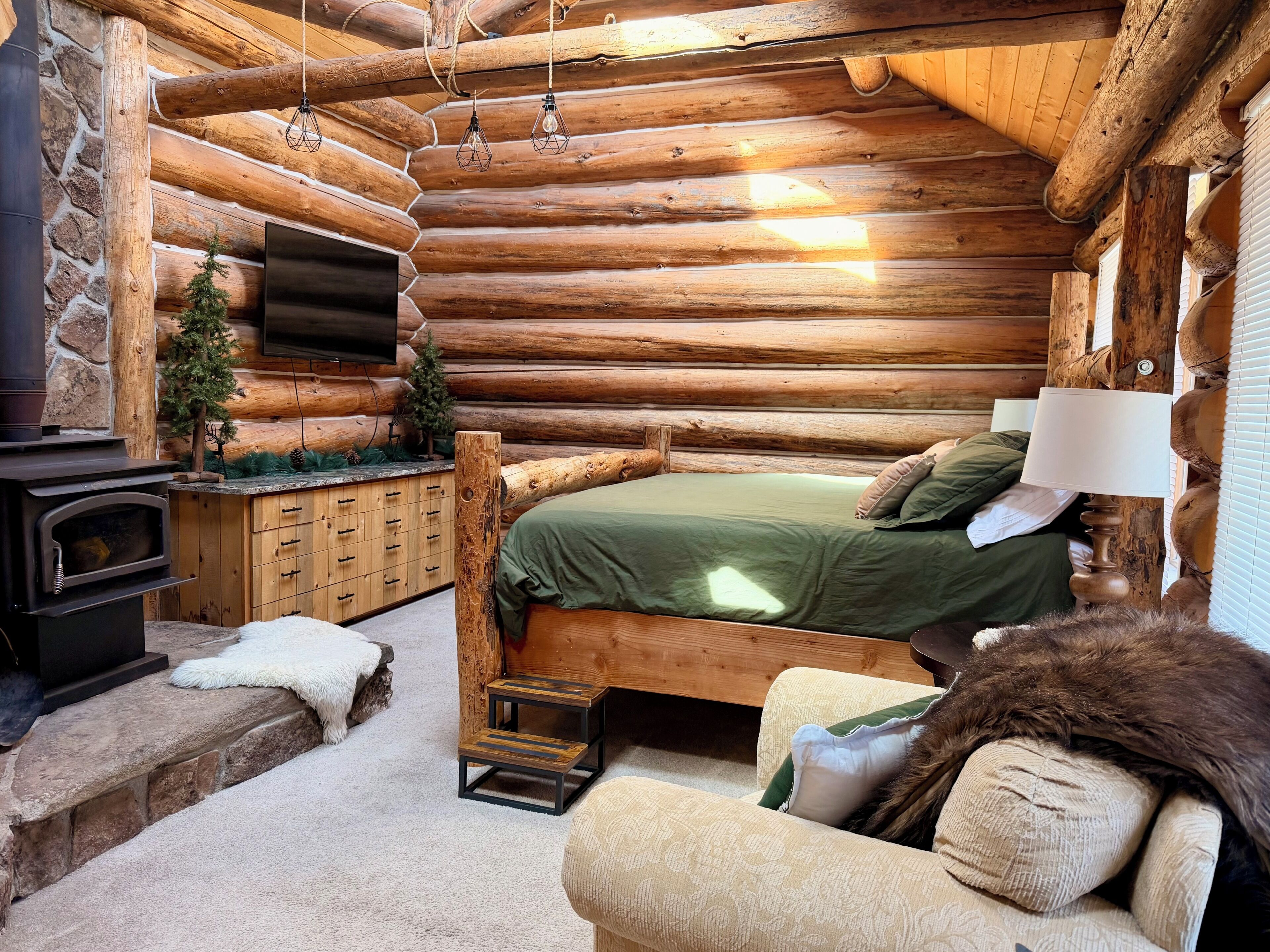 L’intérieur d’une cabane en rondins, avec un lit, une cheminée, une petite table et un canapé.