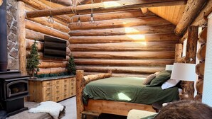 Ein Holzblockhaus-Innenraum mit einem Bett, einem Kamin, einem kleinen Tisch und einer Couch.