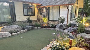 Ein Haus mit einem angelegten Garten, der einen Putting-Green, Steinbeete und verschiedene Pflanzen umfasst.