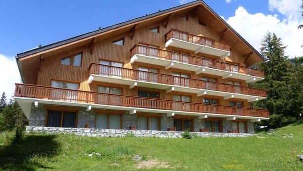 A multi-story wooden building with balconies, set on a grassy slope. - 30m from ski slopes, 3rd floor, view mountain, balcony, tv, ski locker, 58m², Méribel (Méribel - Les Allues)