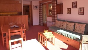 A cozy living room with a wooden dining table, a sofa, and a small wooden stool. - 30m from ski slopes, 3rd floor, view mountain, balcony, tv, ski locker, 58m², Méribel (Méribel - Les Allues)