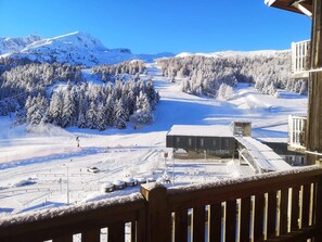 A snowy mountain landscape with a ski resort, including a building with a flat roof and a wooden deck.