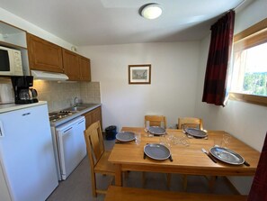 A compact kitchen with a dining table set for four, equipped with basic appliances and a window with curtains. - 50m from ski slopes, 4th floor, view mountain, balcony, tv, 41m², Superdévoluy (Le Dévoluy)