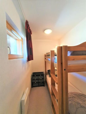 A narrow room with bunk beds, a window with curtains, a radiator, and a black storage unit. - 50m from ski slopes, 4th floor, view mountain, balcony, tv, 40m², Superdévoluy (Le Dévoluy)