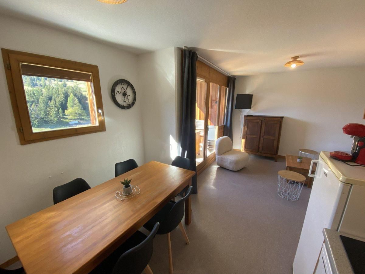 A compact living space with a dining area, kitchenette, and a view of a forest through a window.