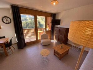 A room with a wooden table, a round coffee table, a sofa, a TV, and a balcony with a view of the outdoors. - 50m from ski slopes, 4th floor, view mountain, balcony, tv, 41m², Superdévoluy (Le Dévoluy)