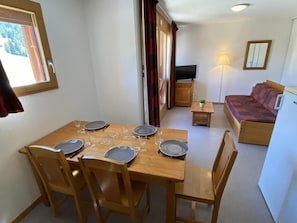 A dining area with a table set for four, a sofa, a television, and a lamp. - 50m from ski slopes, 4th floor, view mountain, balcony, tv, 40m², Superdévoluy (Le Dévoluy)