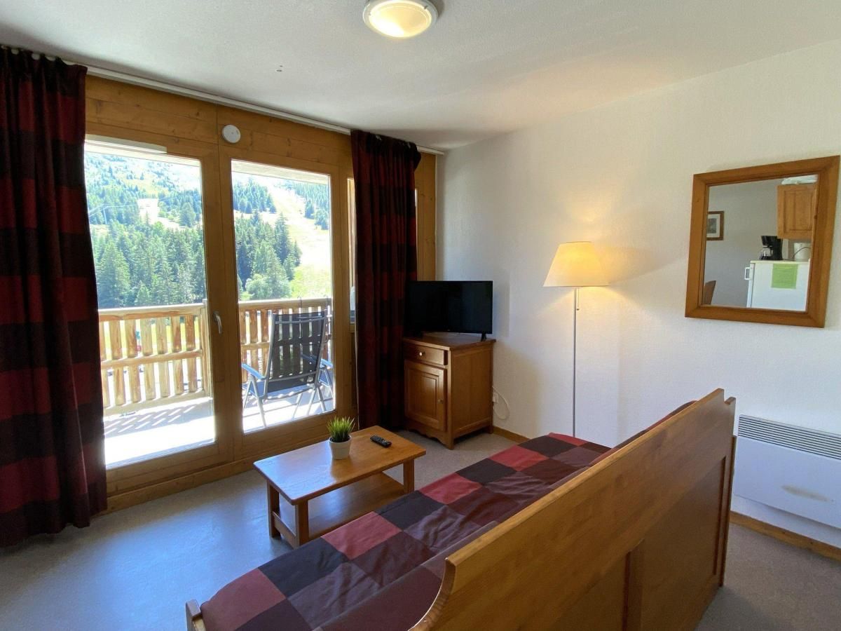 Een gezellige kamer met een bank, een kleine tafel, een televisie en een balkon met uitzicht op bomen.