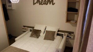 Un llit ben fet amb dos coixins, una taula de nit amb una làmpada i una estant amb un llibre.