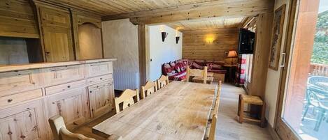 A wooden interior with a long dining table, wooden cabinets, and a cozy seating area.