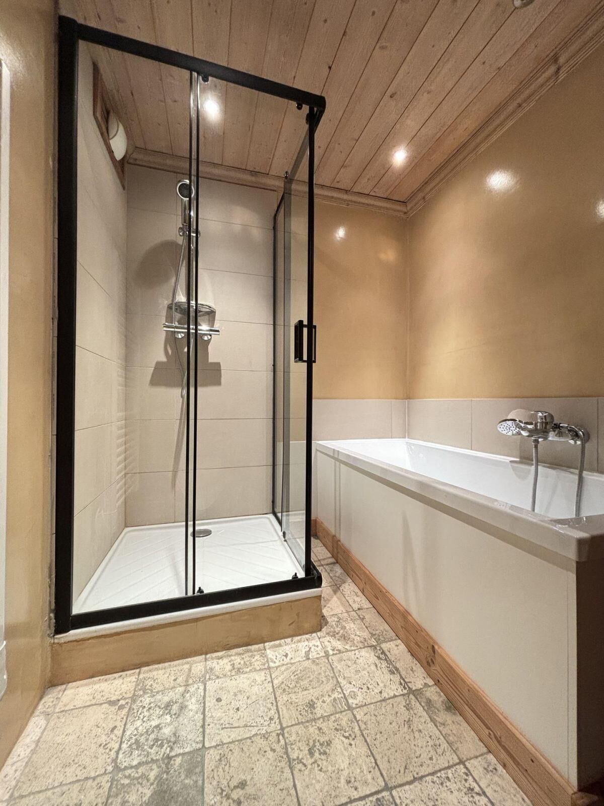 Un baño moderno con ducha envuelta en vidrio, una bañera blanca y techo de madera.