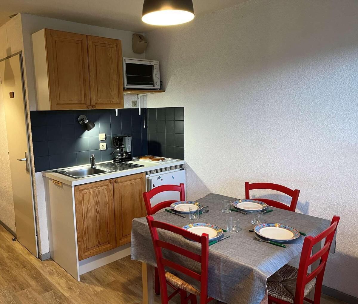 Une cuisine compacte avec des meubles en bois, un four à micro-ondes et une table à manger pour quatre personnes, agrémentée de chaises rouges.