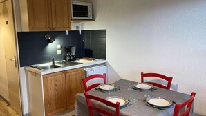 A compact kitchen with wooden cabinets, a microwave, and a dining table set for four with red chairs. - Ground floor, view ski slopes, balcony, tv, 24m², Le Grand Bornand (Le Grand-Bornand)