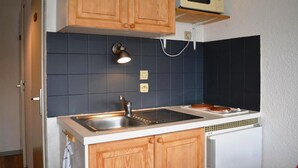 A compact kitchen with wooden cabinets, a stainless steel sink, a microwave, and a tiled backsplash. - Ground floor, view ski slopes, balcony, tv, 24m², Le Grand Bornand (Le Grand-Bornand)