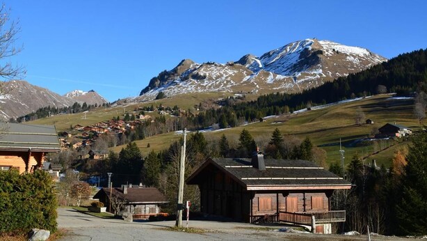 A mountain village with traditional wooden buildings, a clear sky, and snow-capped peaks in the background. - Ground floor, view ski slopes, balcony, tv, 24m², Le Grand Bornand (Le Grand-Bornand)