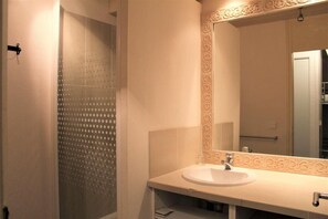 Un baño con un lavabo blanco, un espejo con un marco decorativo y una ducha con puerta de cristal satinado.