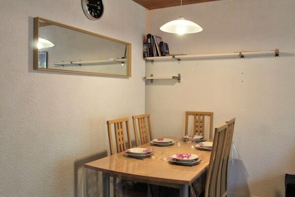 Un comedor con una mesa de madera, cuatro sillas y un espejo en la pared.