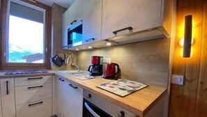 Cocina compacta con microondas, cafetera y hervidor sobre la encimera, armarios de madera y ventana que proporciona luz natural.