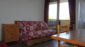Una habitación con un sofá de madera cubierto con un edredón estampado, una mesa de madera y un armario de madera.