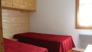 Una habitación pequeña con dos camas individuales, paredes de madera, techo blanco y una ventana con persianas.