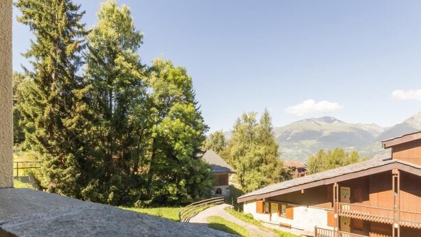 Una cabaña de montaña con fachada de madera, un balcón y vistas al bosque y las montañas circundantes.