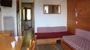 Una habitación compacta con sofá de madera, una mesita con dos tazas, televisor montado en la pared y un espejo sobre el sofá.