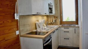 Una cocina compacta con armarios blancos, horno integrado y ventana que aporta luz natural.