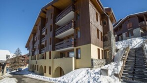 Un hotel de varios pisos con balcones, una pista de esquí al fondo y un cielo despejado.