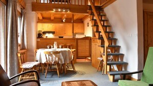 A cozy room with a dining table, chairs, a green armchair, a staircase, and wooden walls. - 100m from ski slopes, 4th floor, balcony, ski locker, 60m², Méribel (Méribel - Les Allues)
