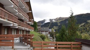 Ein Hotel mit mehreren Balkonen, einer Steintreppe und Blick auf Berge und Bäume.