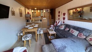 Ein gemütliches Wohnzimmer mit einer Couch, einem Esstisch und einer Küchenzeile im Hintergrund.