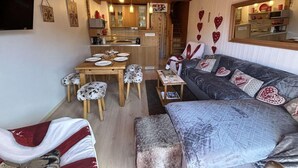 Ein gemütliches Wohnzimmer mit einer Couch, einem Esstisch mit Stühlen und einer Küchenzeile im Hintergrund.