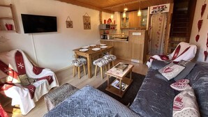 Ein gemütliches Wohnzimmer mit einer Couch, Sesseln, einem Esstisch und einer Küchenzeile.