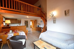 Ein gemütliches Zimmer mit einer Holztreppe, einer Essecke mit Tisch und Stühlen sowie einem Bett mit gemusterten Textilien.
