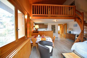 A cozy cabin with a dining area, kitchen, and a loft bedroom with a wooden staircase.