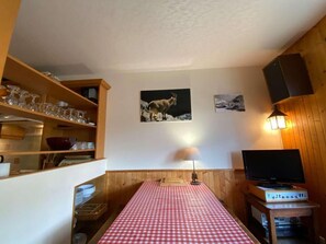 Una habitación acogedora con una mesa a cuadros, estantes de madera, un televisor y obras de arte colgadas en la pared.