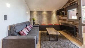 Una sala moderna con un sofá gris, un banco de madera y una pared de piedra.