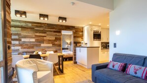 Una sala de estar moderna con sofá, un comedor con sillas, una cocina con electrodomésticos y una pared de madera.