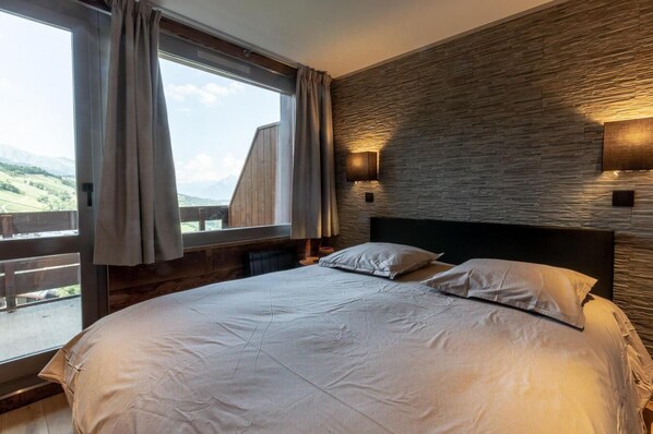 A bedroom with a large bed, a view of the outdoors, and a stone wall.