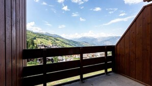 Un balcón de madera con baranda metálica que da a un paisaje montañoso con edificios.