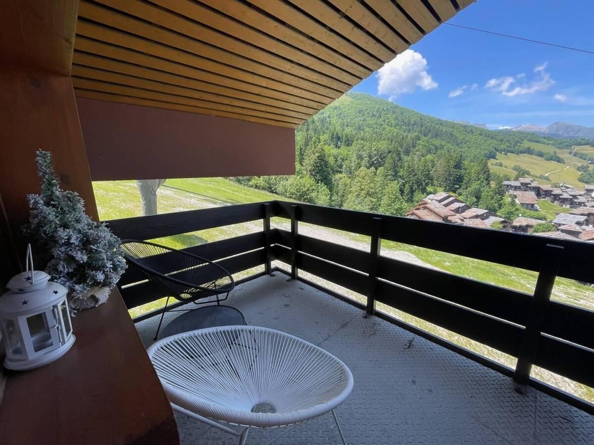 A balcony with a view of a village, a white chair, and a white lantern.